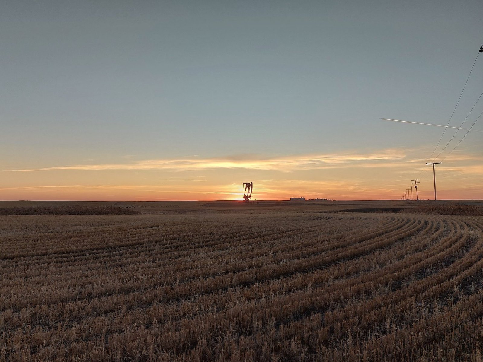 A distant pumping unit on the horizon of a stubble field at sunset