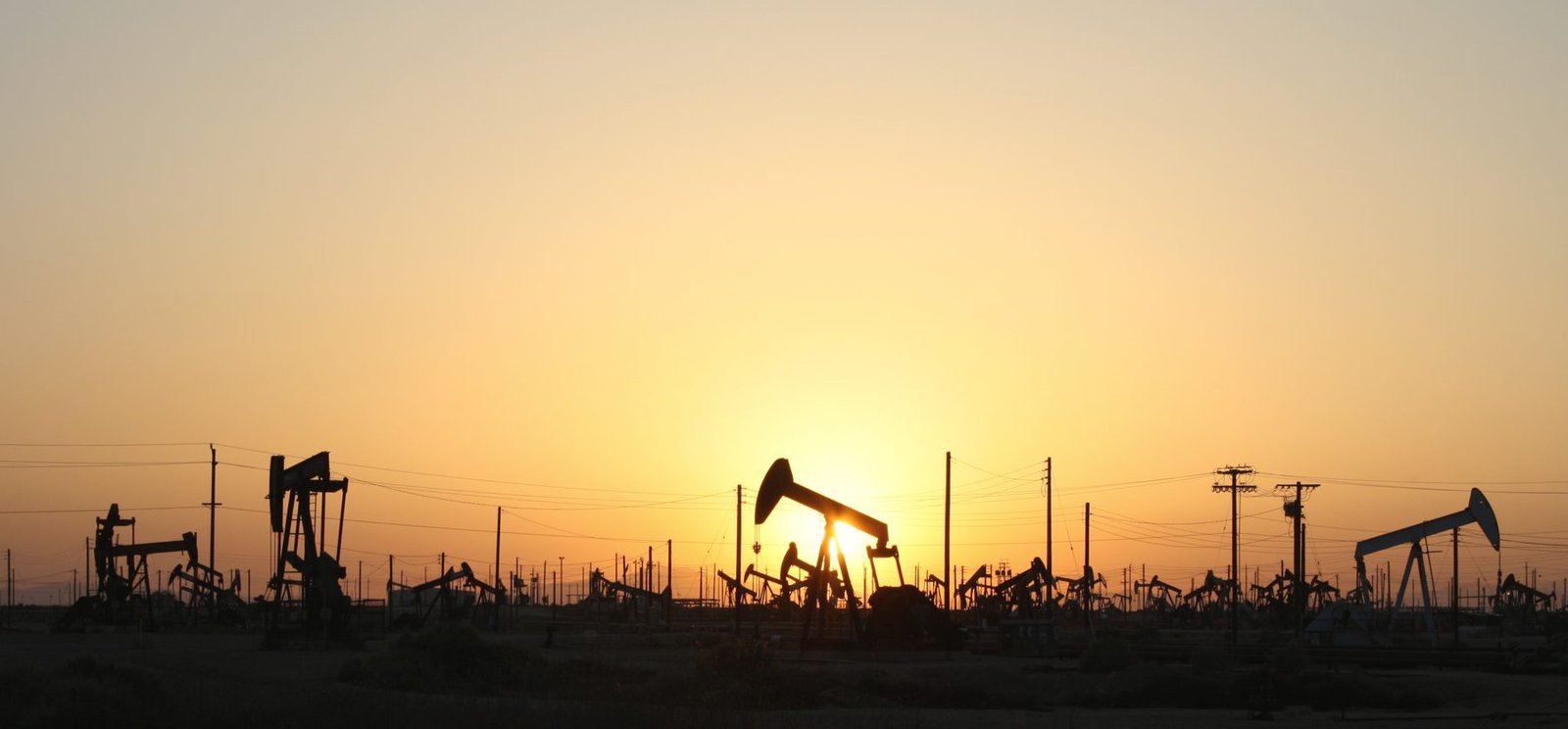 Many pumping units silhouetted against an orange sunset